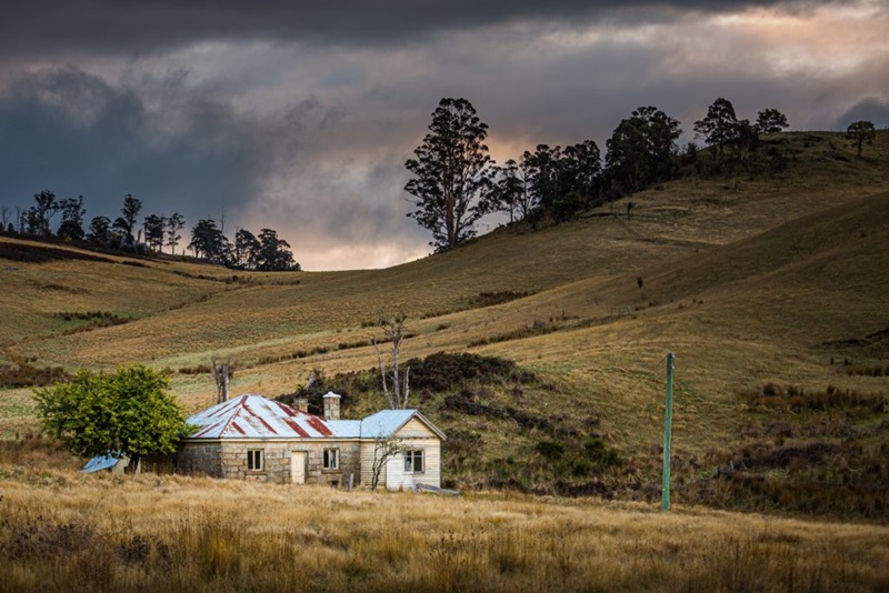 Old farm house nestled into the side of a hill with stormy clouds in the background. 