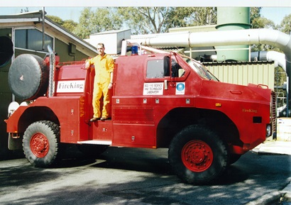 A person dressed in yellow coveralls on board a red fire truck.