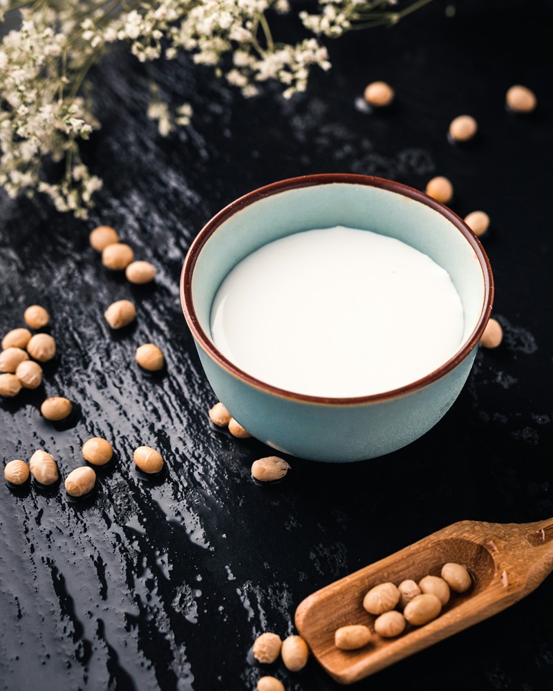 A cup of soy milk with soy scattered around it. 
