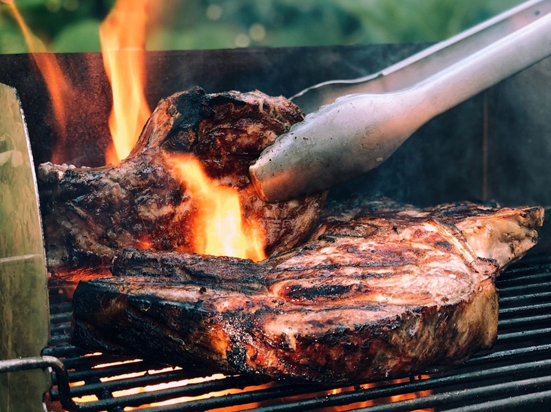 Steak is turned with tongs on BBQ