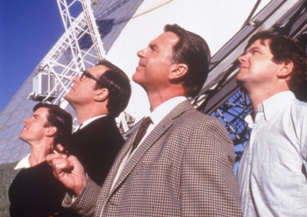 Scene from The Dish movie where four people are standing in front of a radio telescope dish looking up into the sky. 