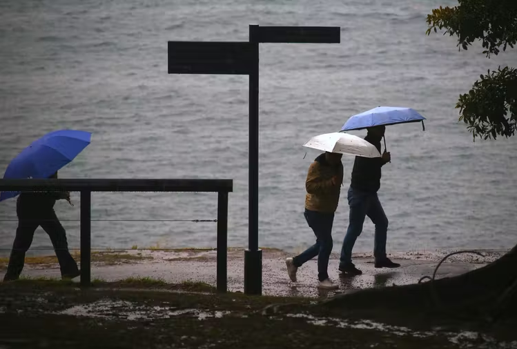 Three people walking along a beach with umbrellas. Climate change weather