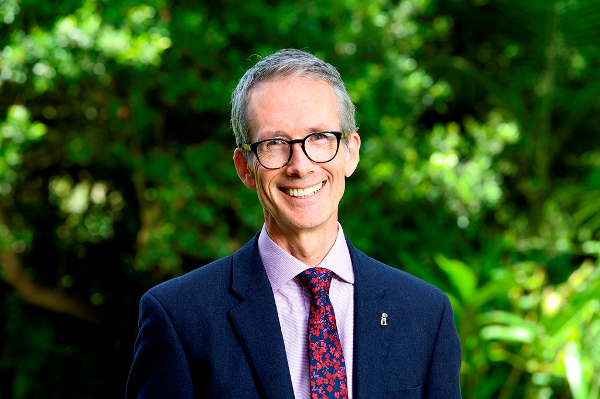 Man with glasses, jacket and tie with plants in background