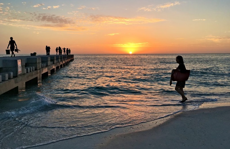 A sillouhette of a person walkin alongside the beach at sunset.