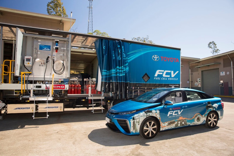 car next to large truck with hydrogen gas bottles, ready to refuel car