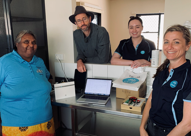 A group of four people, smiling at the camera surroundinig a laptop. Two of the people pictured are CSIRO researchers in polo shirts.
