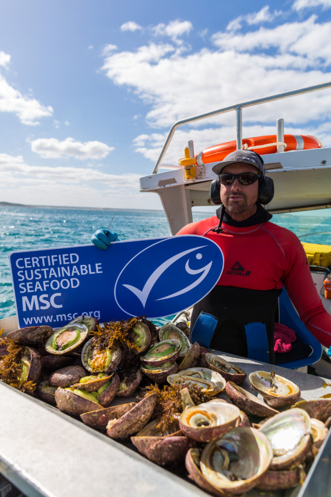 Abolone fisher holds MSC sign above crate of catch