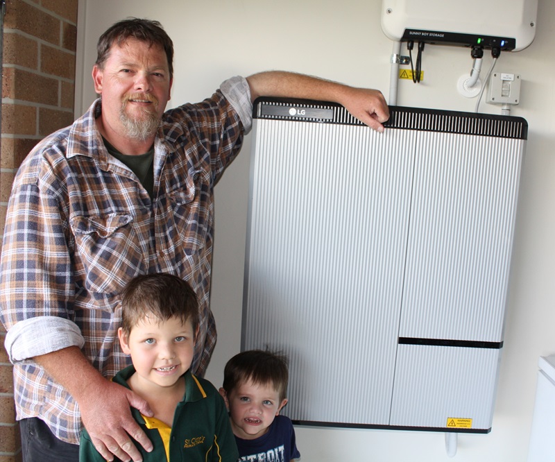 father with two small children standing in front of home solar battery
