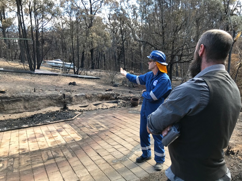 two men standing near burned remains of a house