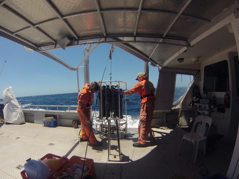 two people in orange boiler suits handling a carousel of cannisters on boat deck