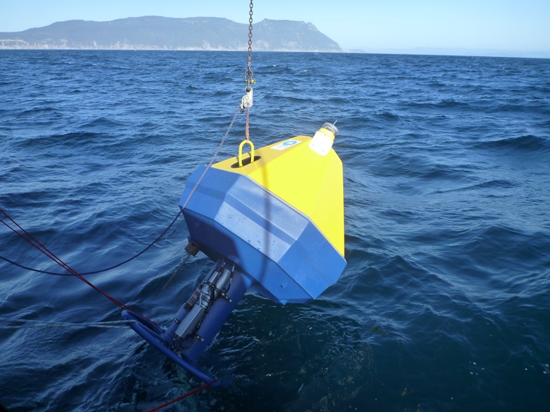 bright yellow and blue capsule being lowered into the ocean with an island in the distance