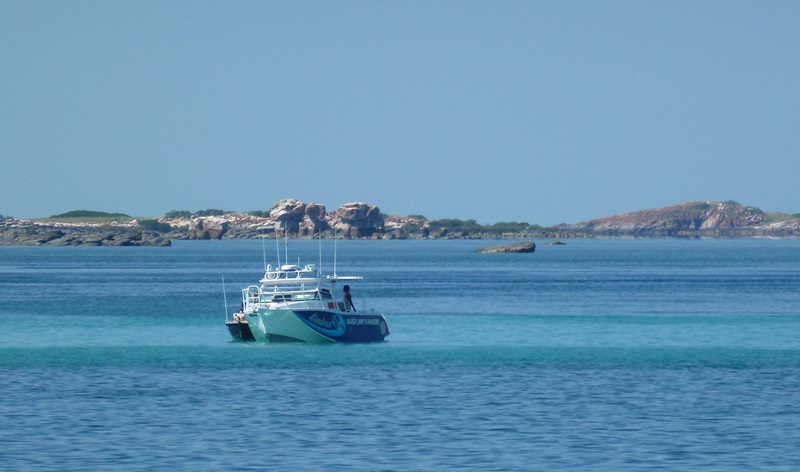 Small boat floating on bright blue sea with rocky peninsula in background