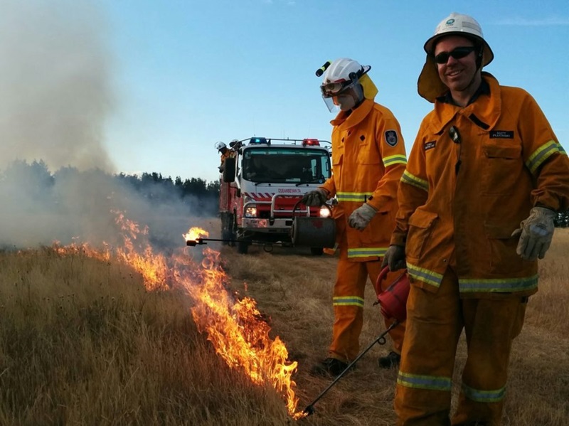 Two people in protective clothing by a fire