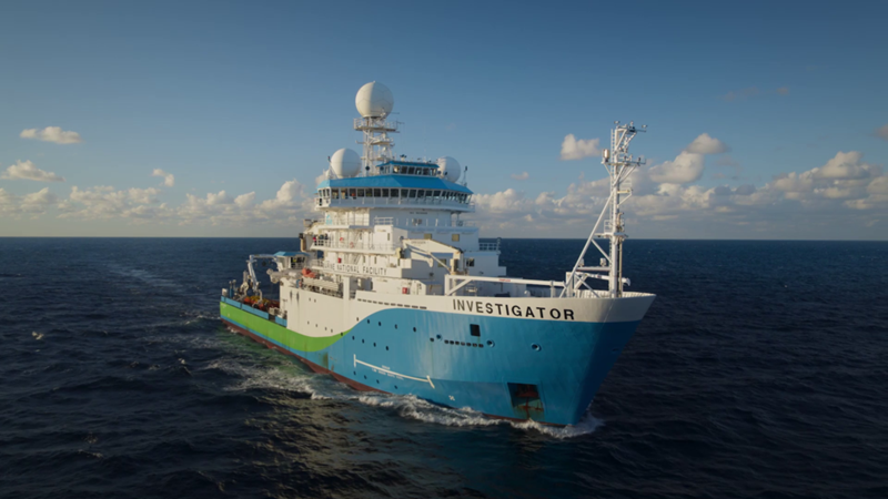 A blue, green and white painted research vessel on the open ocean.