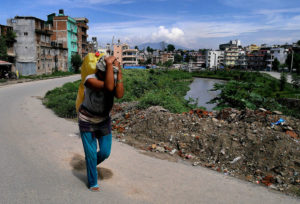 Woman carrying plastic containers of water on her back beside river