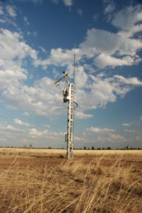 A tall metal tower with instruments near the top in a paddock