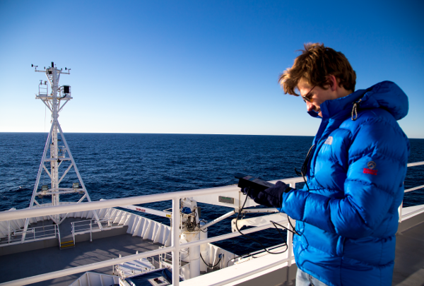 man in blue puffer onboard ship checking handheld monitoring device