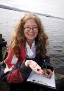 A woman holding up a small sea star with clipboard