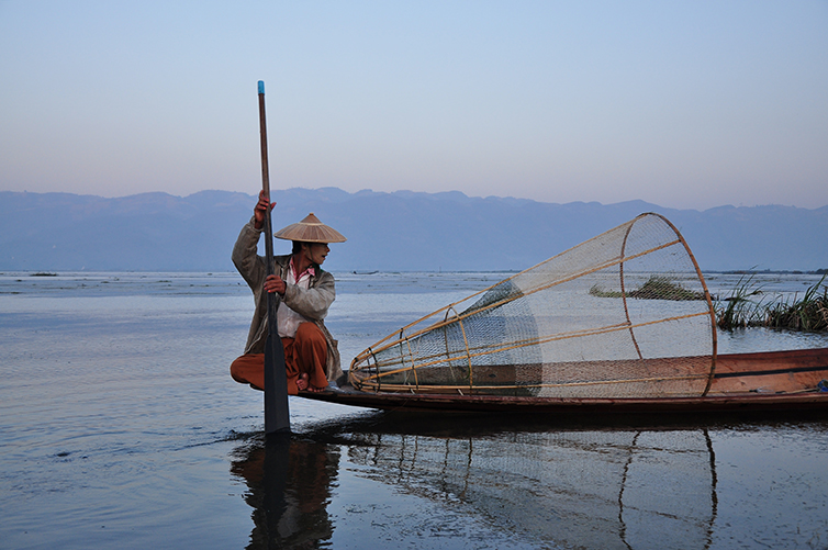 Man in a fishing canoe on a lake with traditional fishing net