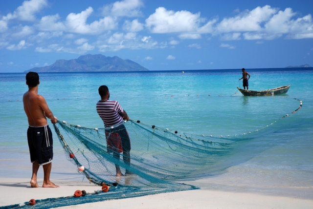 Fishers standing on shore holding a fihsing net, with a boat in the background