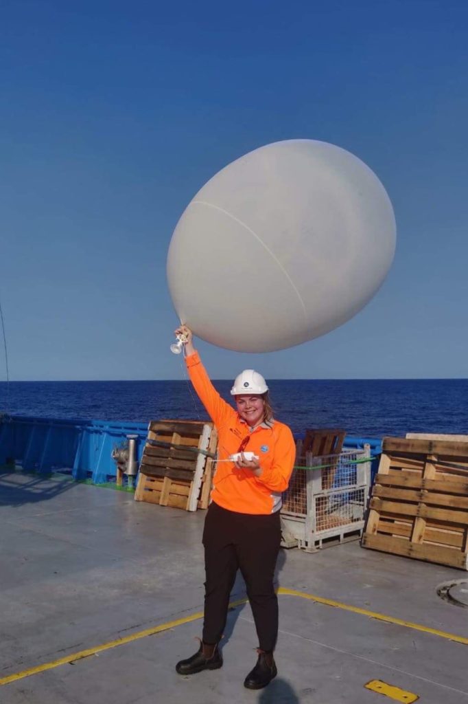 A person standing on the deck of a ship holding a weather balloon.