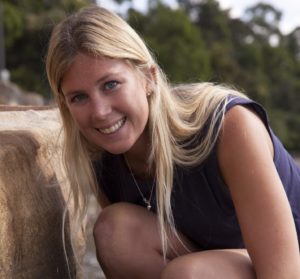 A female scientist crouched near a rock on a beach, smiling