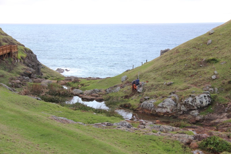 Two scientists in a valley doing research, with the ocean in the background