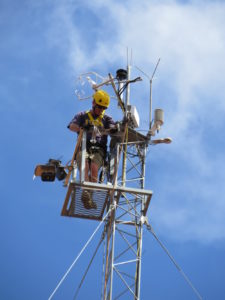 Man working in high tower with instrumentation against blue sky