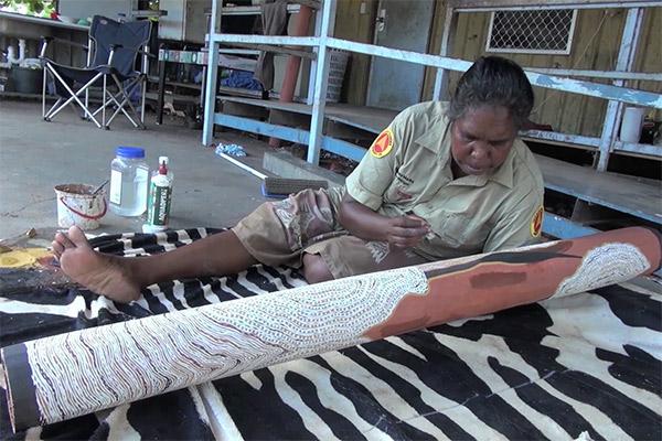 A female Indigenous artist painting a log