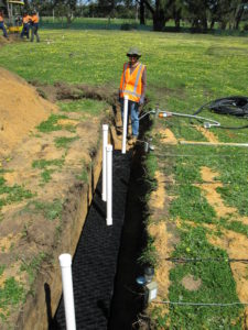 A person standing in a shallow trench lined with plastic crates and pipes emerging