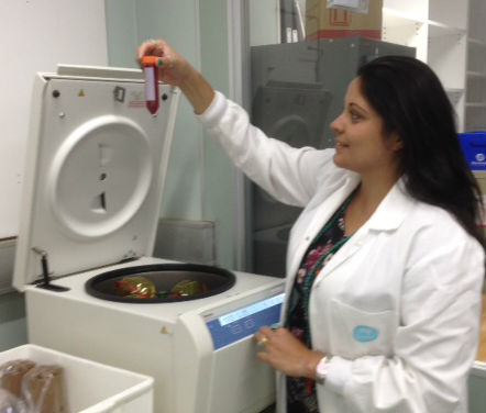 person in a white coat lifting the lid on a piece of equipment in a lab