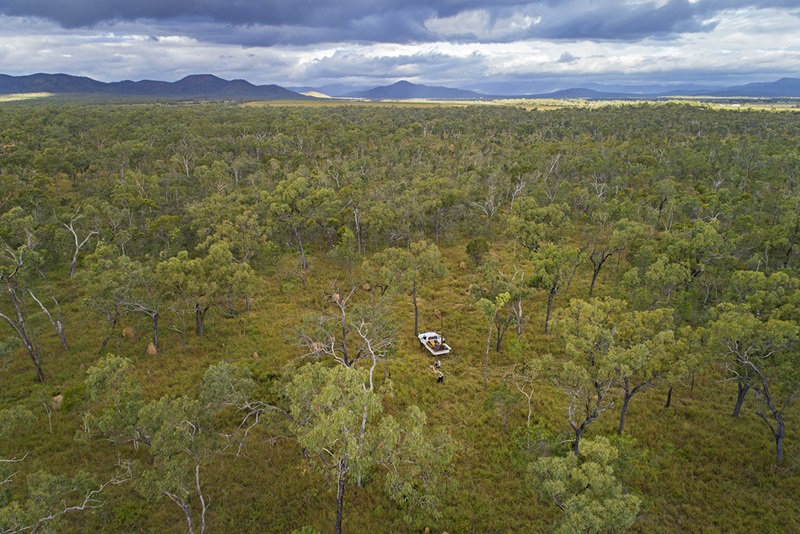 Aerial photo of bush with people and truck with a drill rig attached, and mountains in the distance