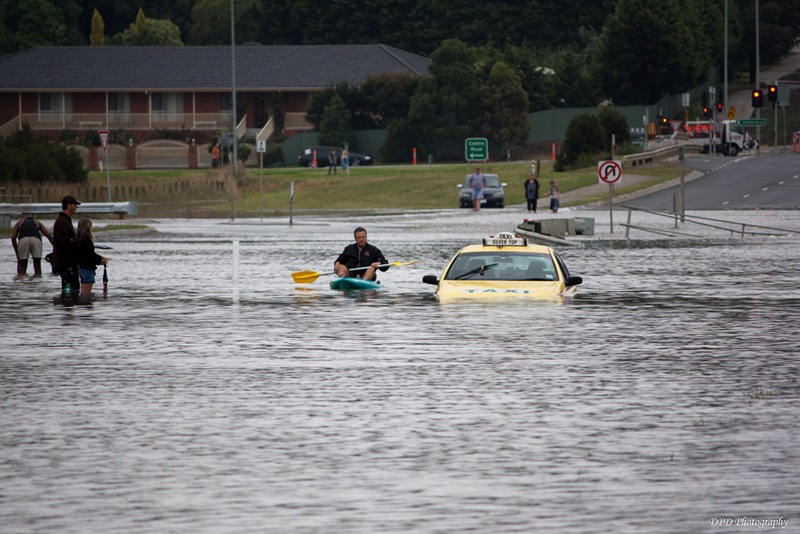 Flooded road with stranded taxi underwater and man paddling kayak on water