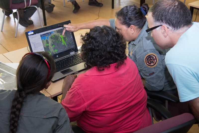 group of four people looking over a lap top showing Google Earth map