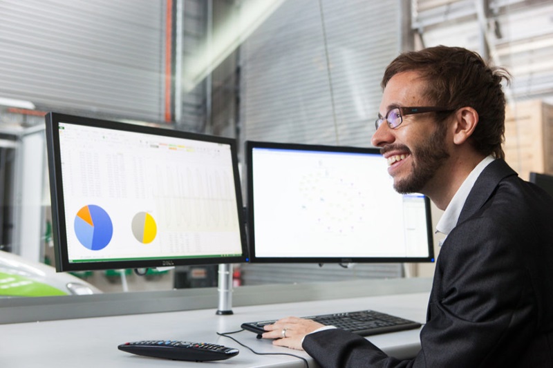 man in suit looking at two computer screens showing pie charts