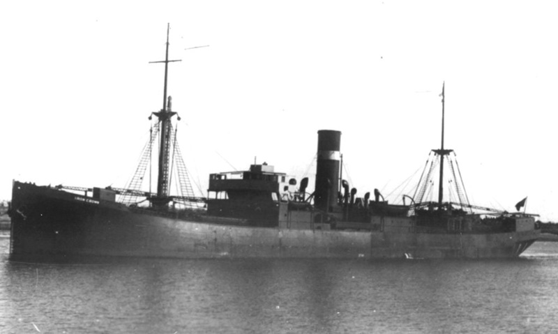 A historical black and white photo showing a merchant steamship near a coastline.