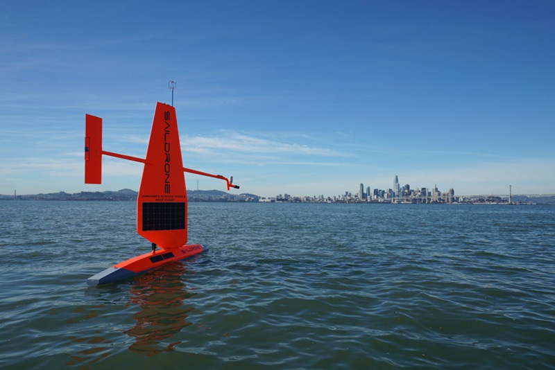red sail-like object on ocean with city in the background
