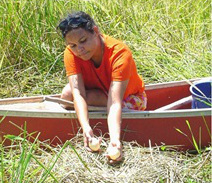 woman in orange tshirt in a canoe among reeds holding two eggs above a bird nest