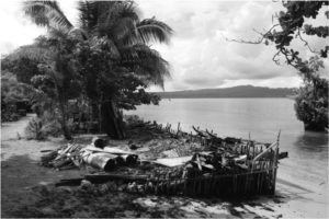 Black and white image of a low wall along waters edge of beach