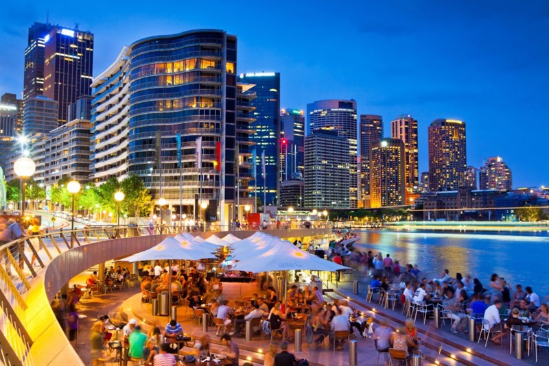 A city setting lit up at night with people dining by the water