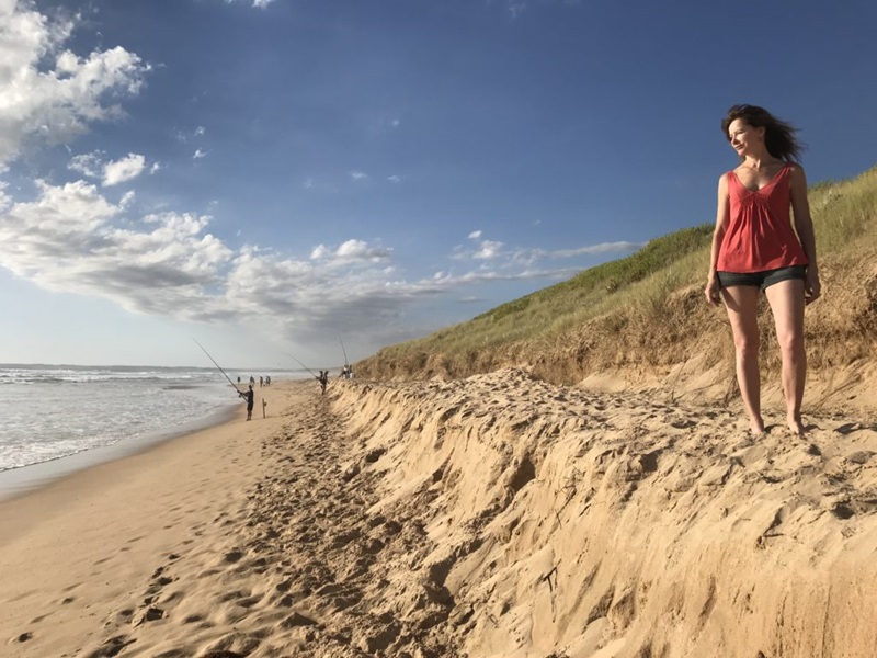 A woman standing on a raised level of sand, gazing out at the horizon