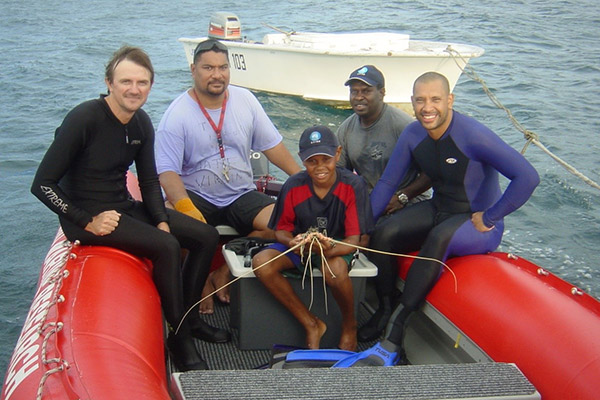 Four men and a boy (holding a lobster) in an inflatable red boat