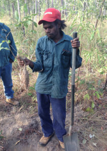 Man holds a root vegetable up and leans on shovel