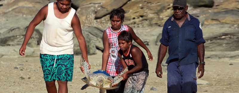 Three children carry a turtle followed by a man in a dark blue uniform