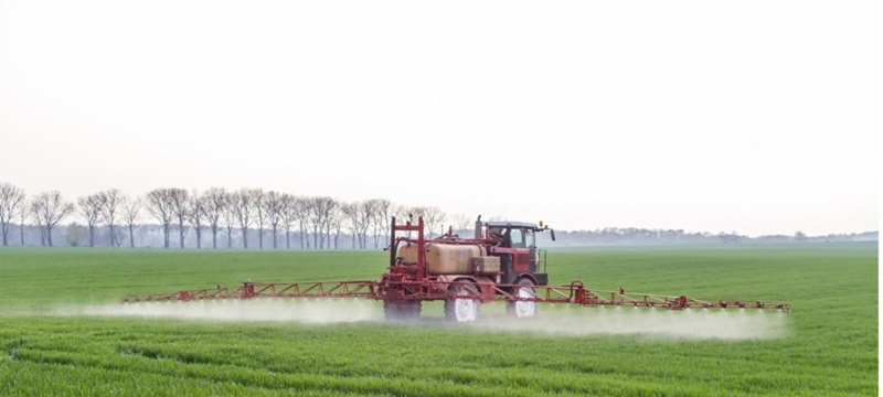 An agricultural tractor spraying a field of crops.