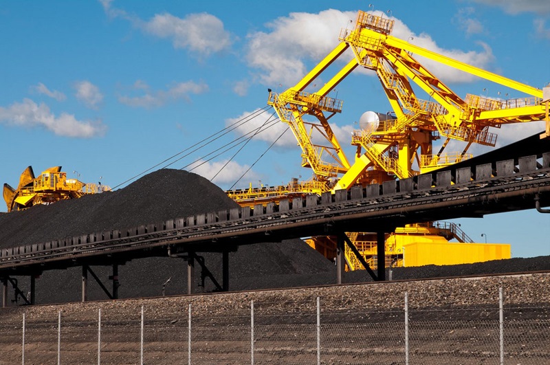 A large mound of coal with yellow machinery behind it