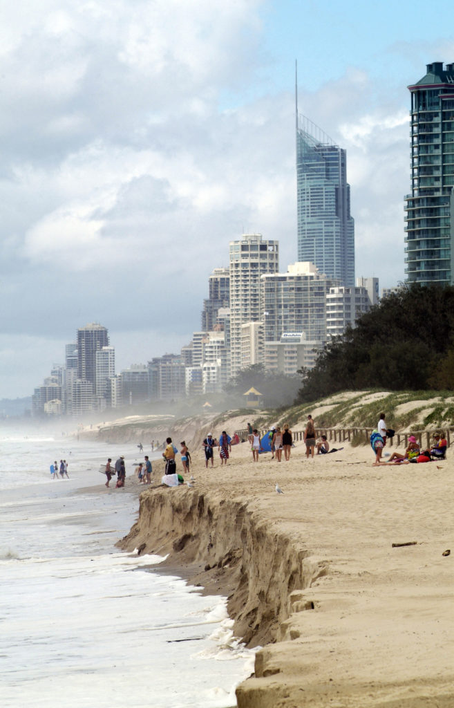 People standing on a badly eroded coast line. The image shows the effects of a king tide on Queensland’s Gold Coast beachfront.