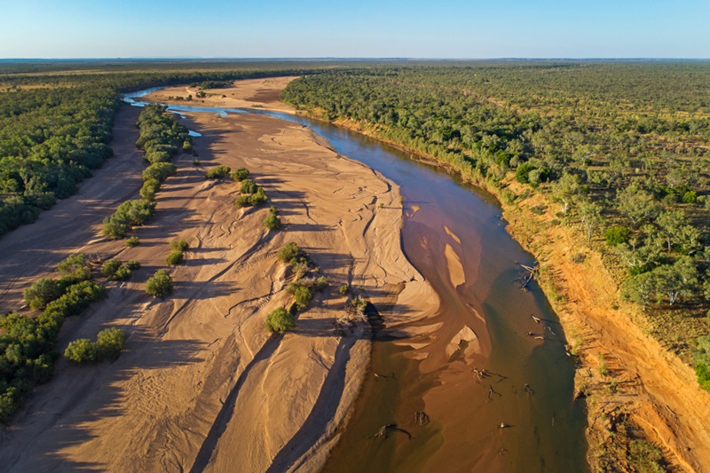 aerial photo of a sandy river bed with some water flow and riparian bushland