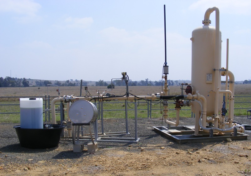 A large cylinder and with pipes coming from the ground in a paddock