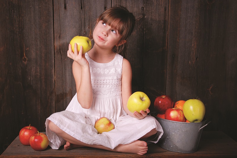A young girl eating an apple next to a bucket of apples